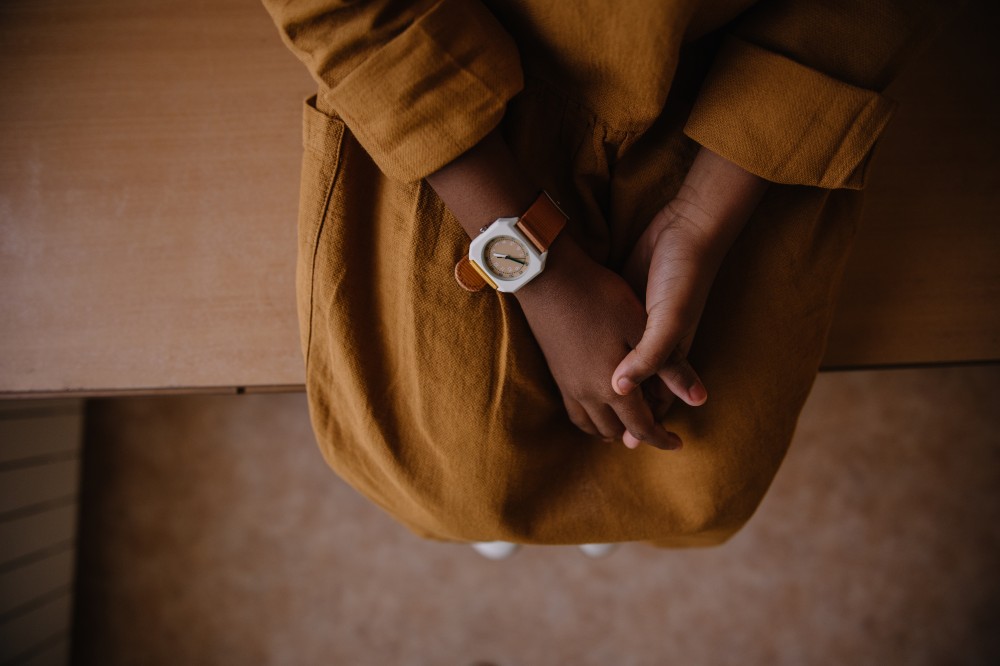 A child sat on a wooden seat in a mustard coloured dress wearing a watch