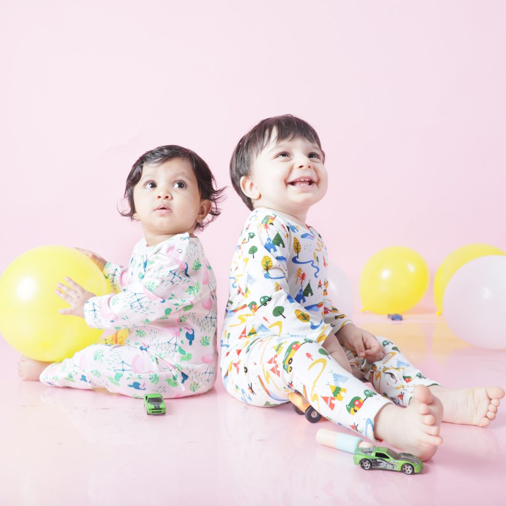 Two young children sat on the floor in babygros holding yellow balloons 