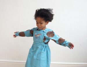 A young girl in a pale blue dress holding her arms out