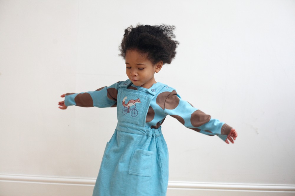 A young girl in a pale blue dress holding her arms out