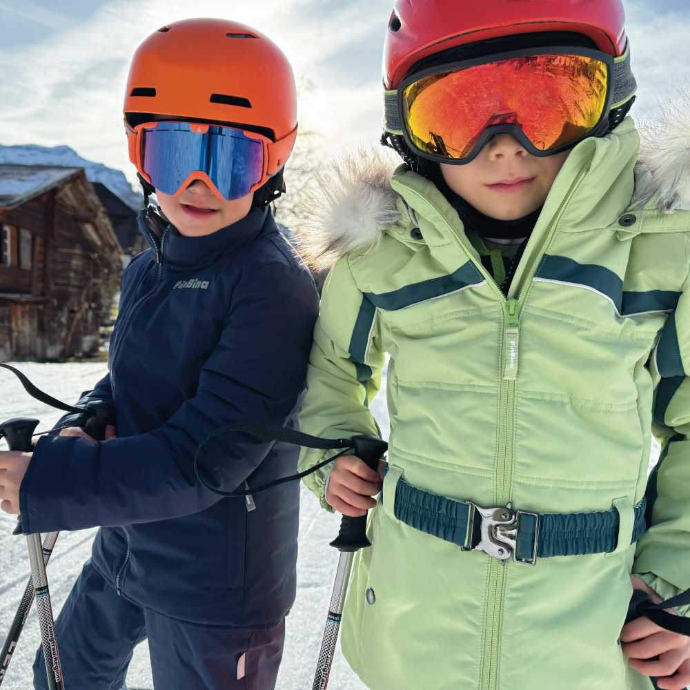 Two childen on a ski slope wearing skiwear, ski goggles and helmets 