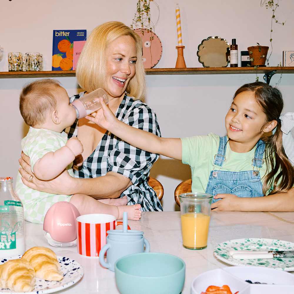 A woman holding a baby sat at a kitchen table beside a young girl 