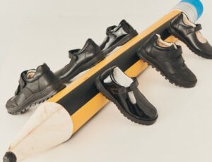 Children's black school shoes displayed on a large pencil