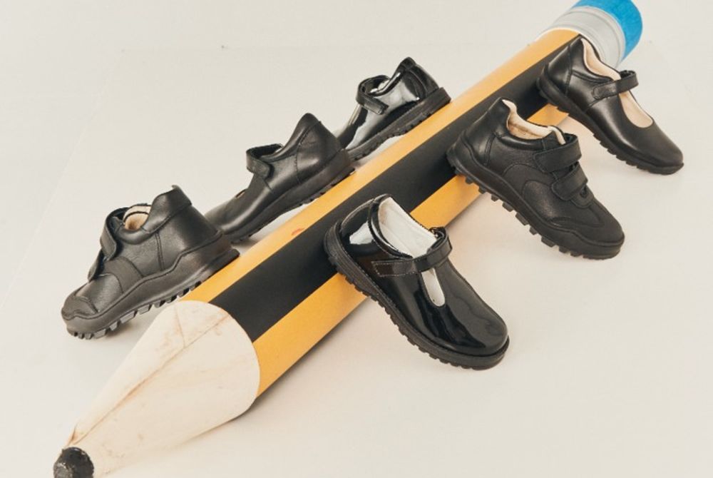 Children's black school shoes displayed on a large pencil