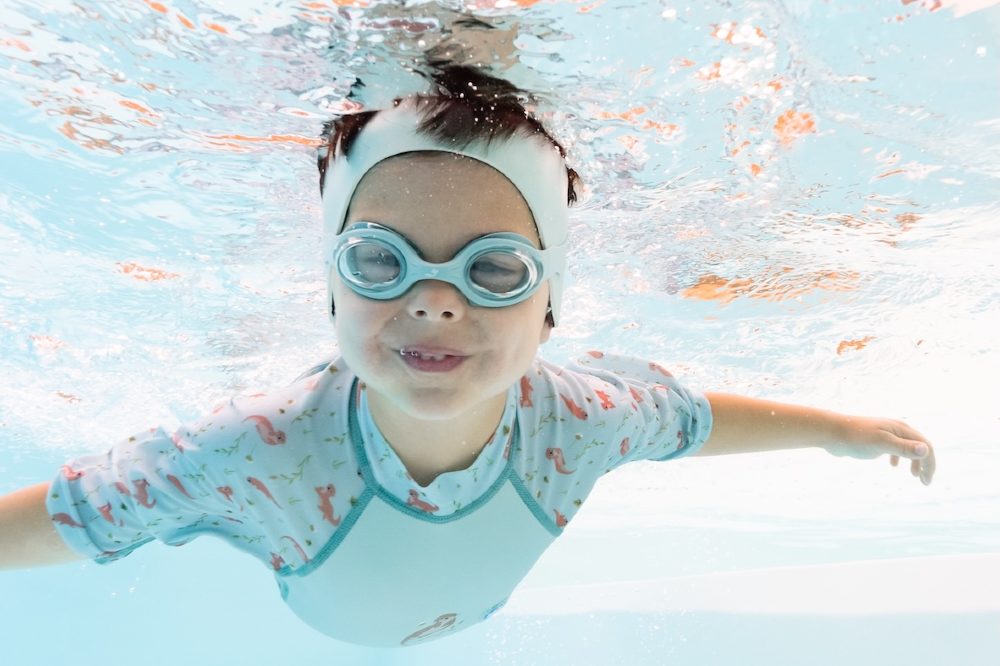 A child underwater in a pool wearing swimming goggles and a ear band by Splash About