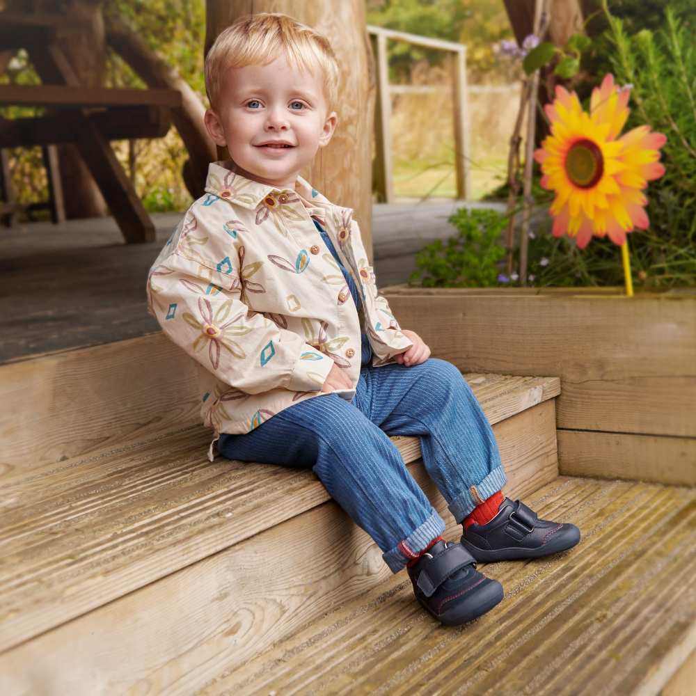 A young boy sat on a wooden step outside beside a flower decoration 