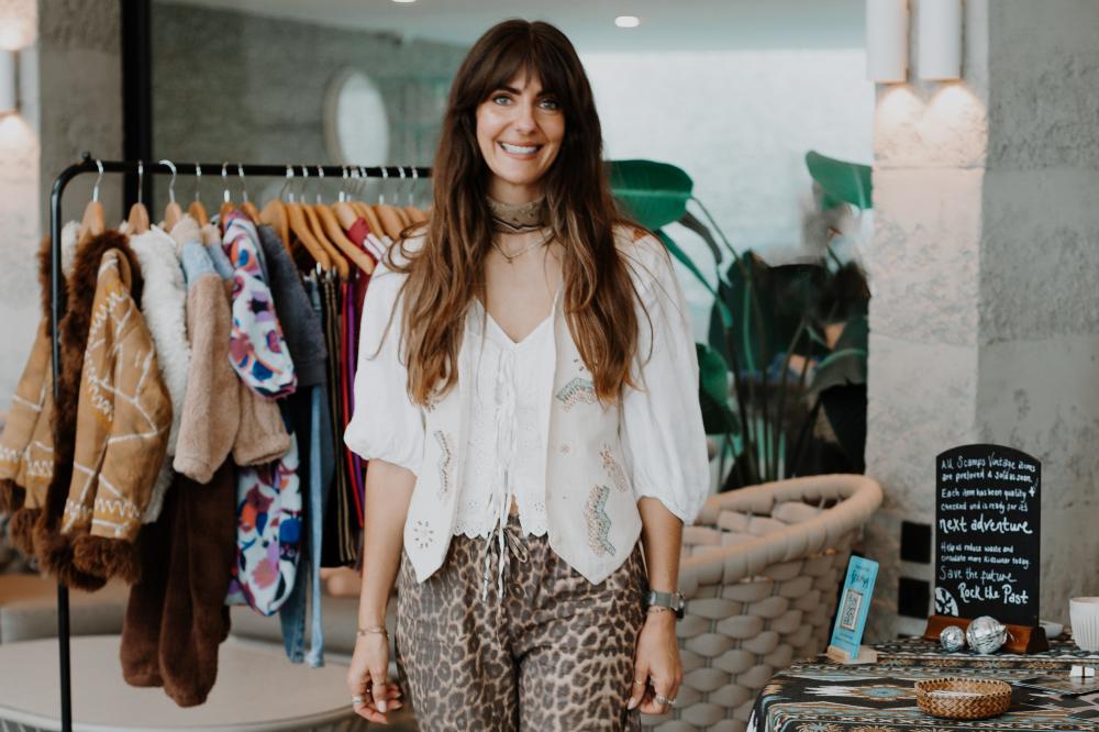 Lauren Cooley founder of The Preloved Club stood in a room beside a table and rail of preloved children's clothes