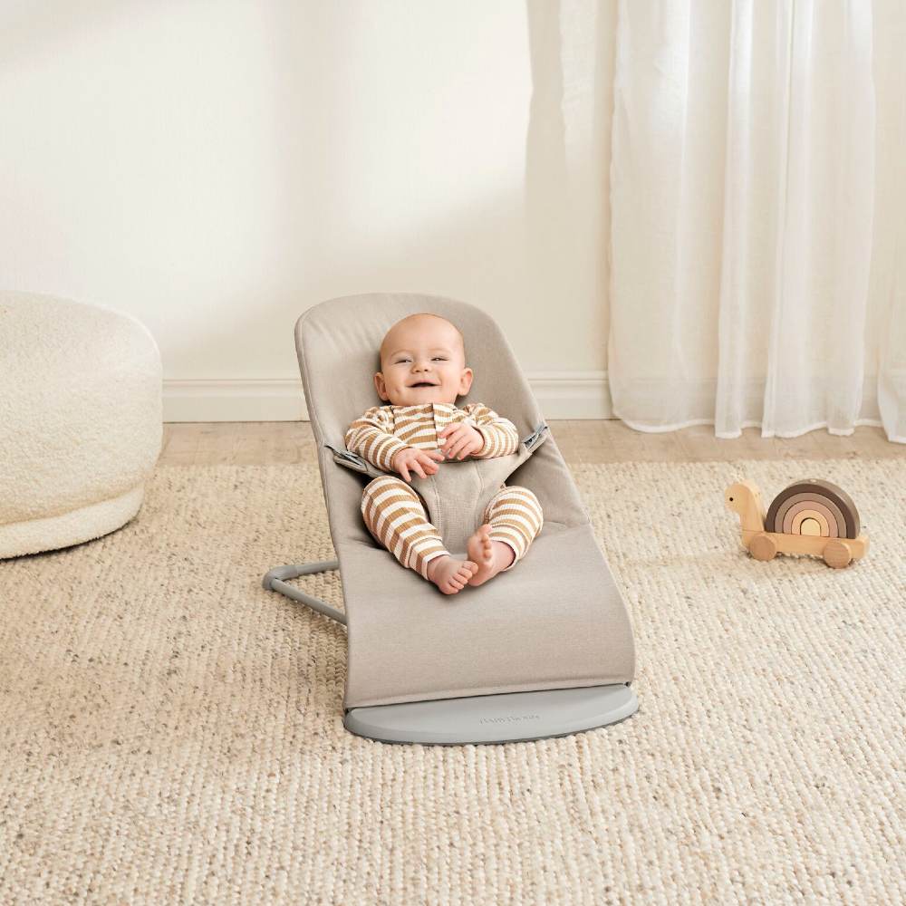 A baby shown in a room sat in a baby bouncer by BabyBjorn 