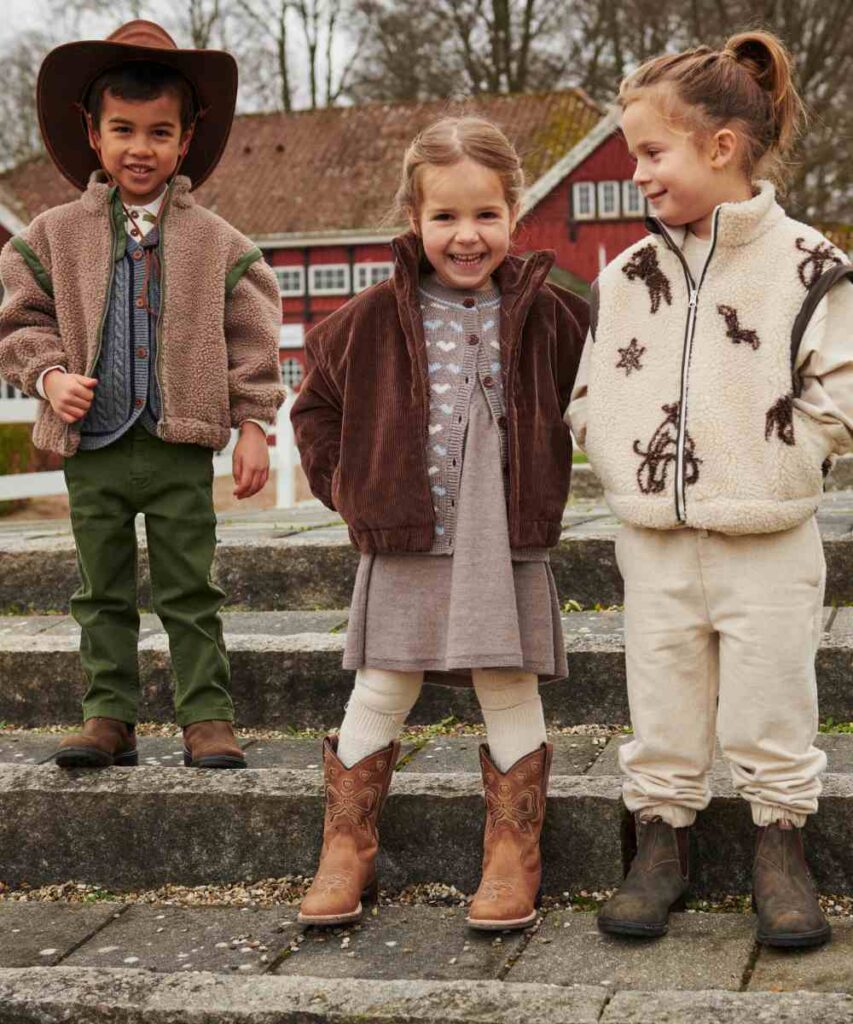 Three young children stood outside on some steps wearing western inspired winter outfits 