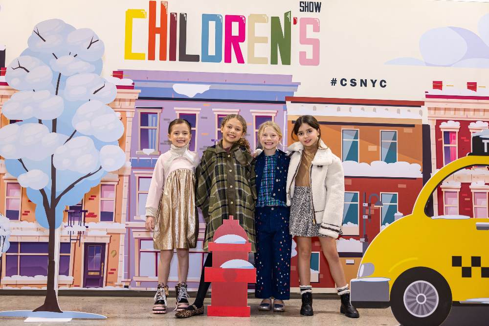 Four children stood in front of a New York street illustration with the words Children's Show above it