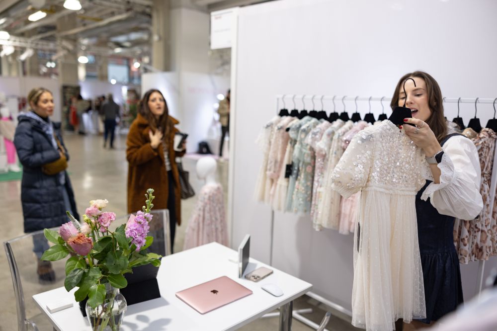 A woman on a stand at the Children's Show holding up a girl's sparkly dress to show buyers 