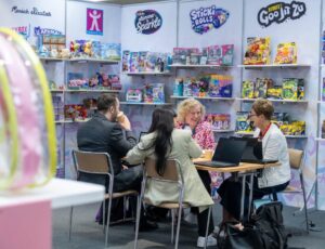 A group of four people sat at a table on an exhibition stand displaying toys at the INDX Toys Show