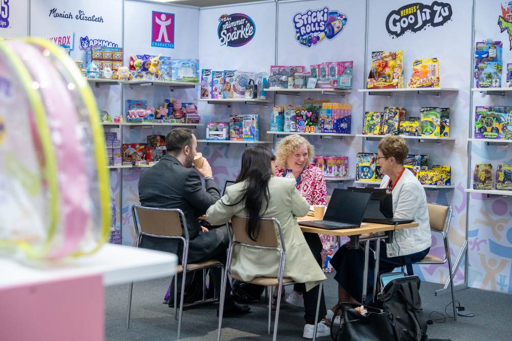 A group of four people sat at a table on an exhibition stand displaying toys at the INDX Toys Show