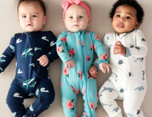 Three babies lying in a row wearing printed babygros by Kyte Baby