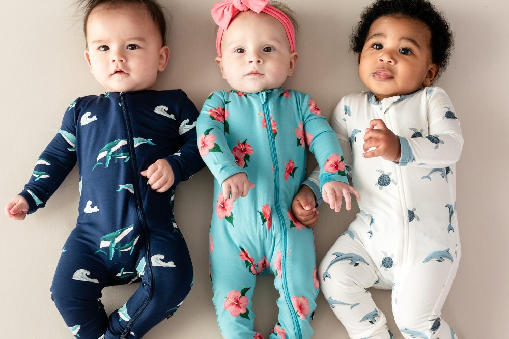 Three babies lying in a row wearing printed babygros by Kyte Baby