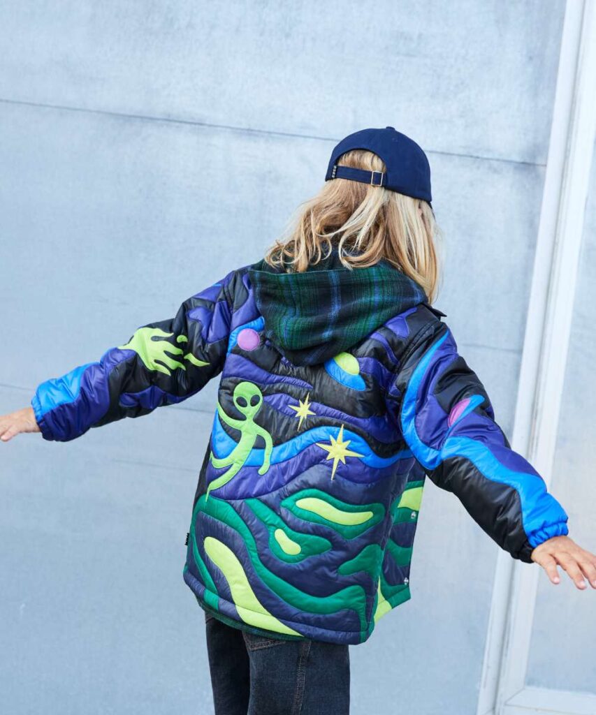 The back of a child with the arms out wearing a blue cap and a coat with space motifs on it 