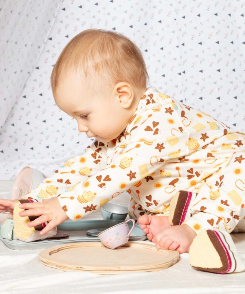 A baby sat on the floor playing with a toy cake and tea set 