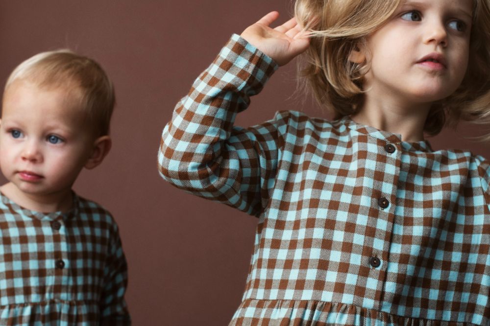 Two children in brown and blue checked outfits against a brown background