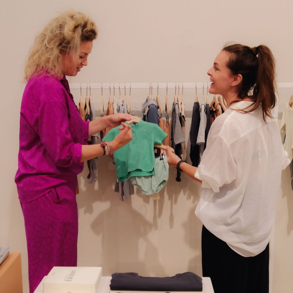 Two women on a trade show stand looking a childrenswear garments 