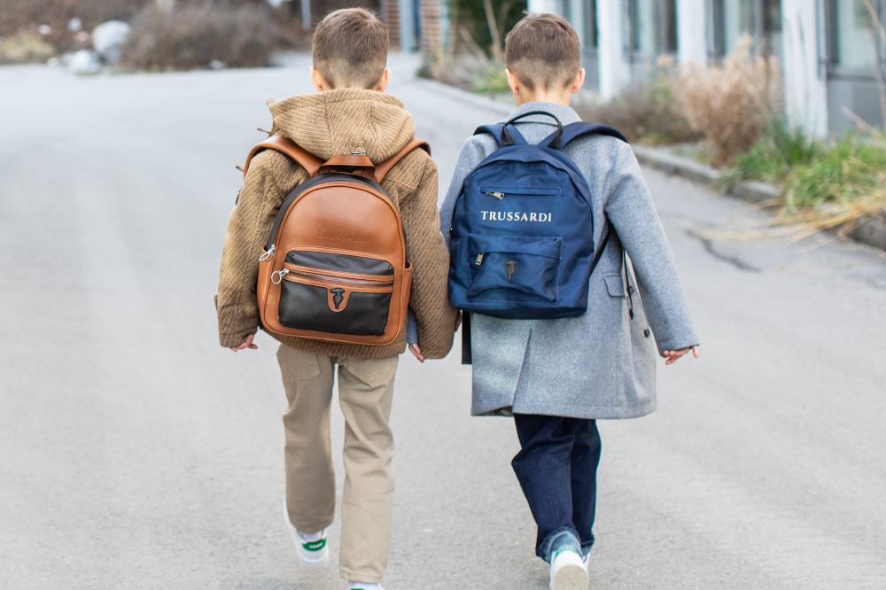 The back of two boys holding hands with rucksacks on their backs 