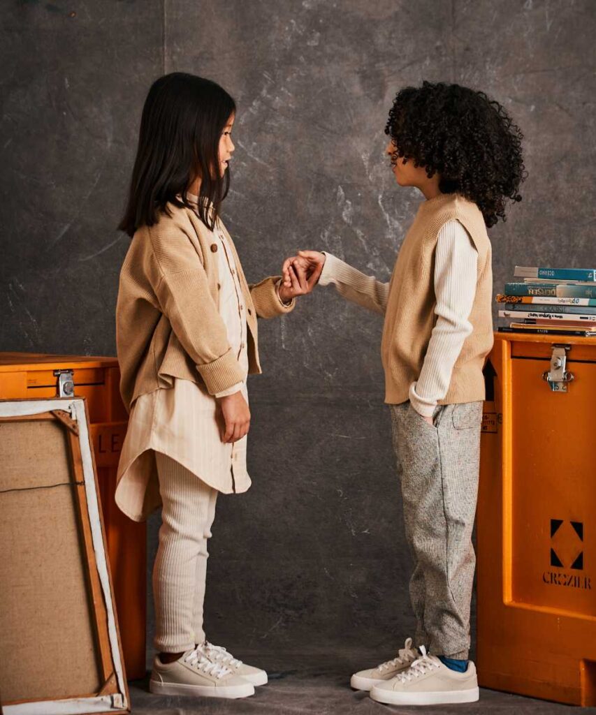 Two children facing each other holding hands in front of a chalk board 