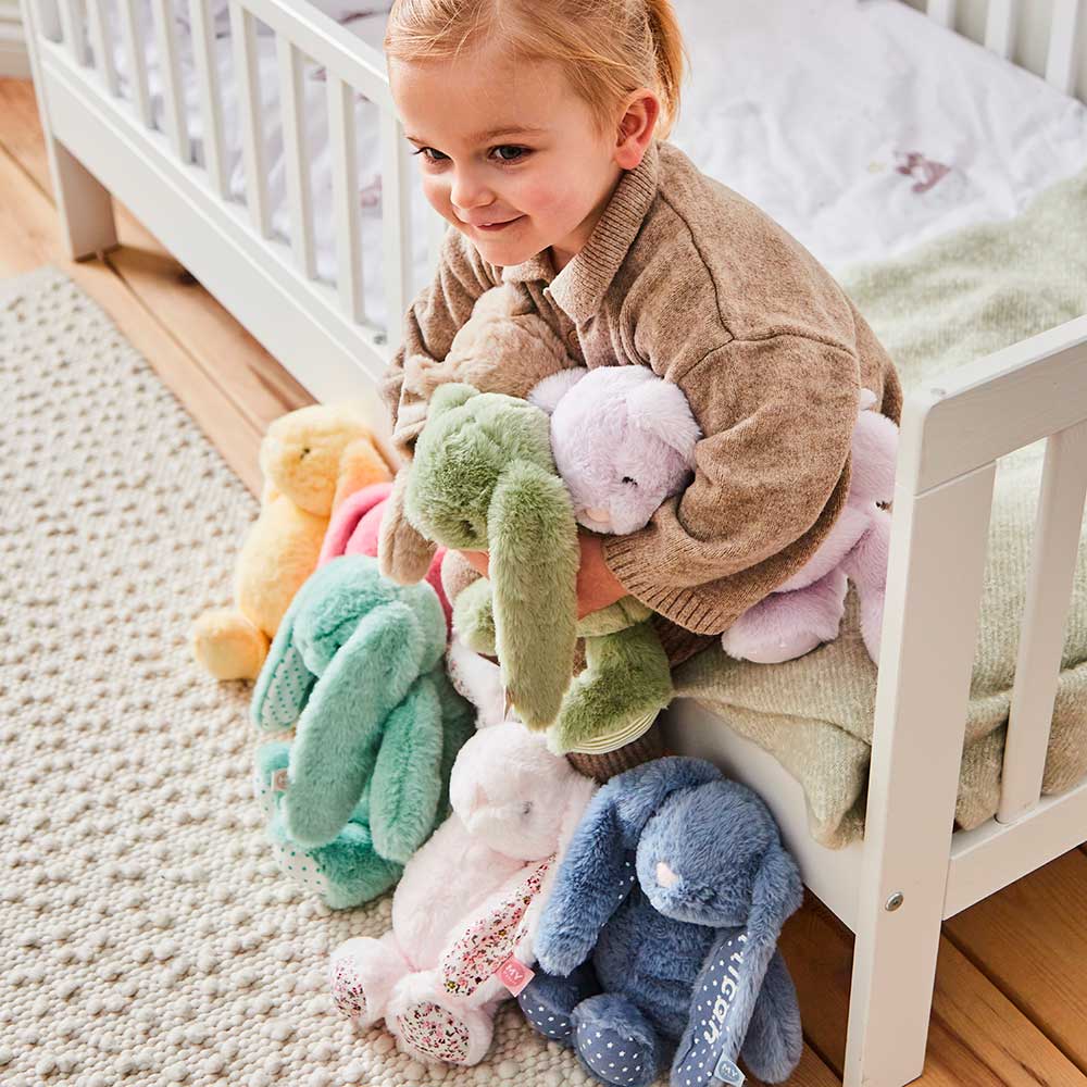 A young girl holding multiple soft toy bunnies in multiple colours