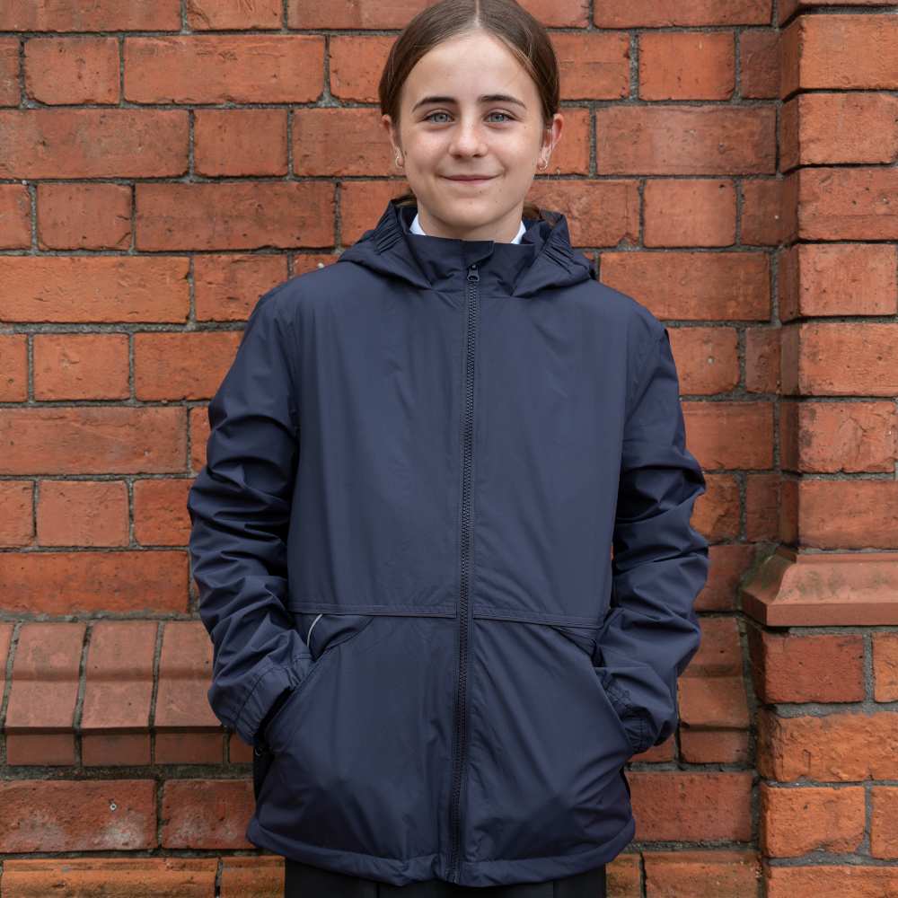 A girl stood against a brick wall wearing school uniform and The Anorak coat by 1880 Club