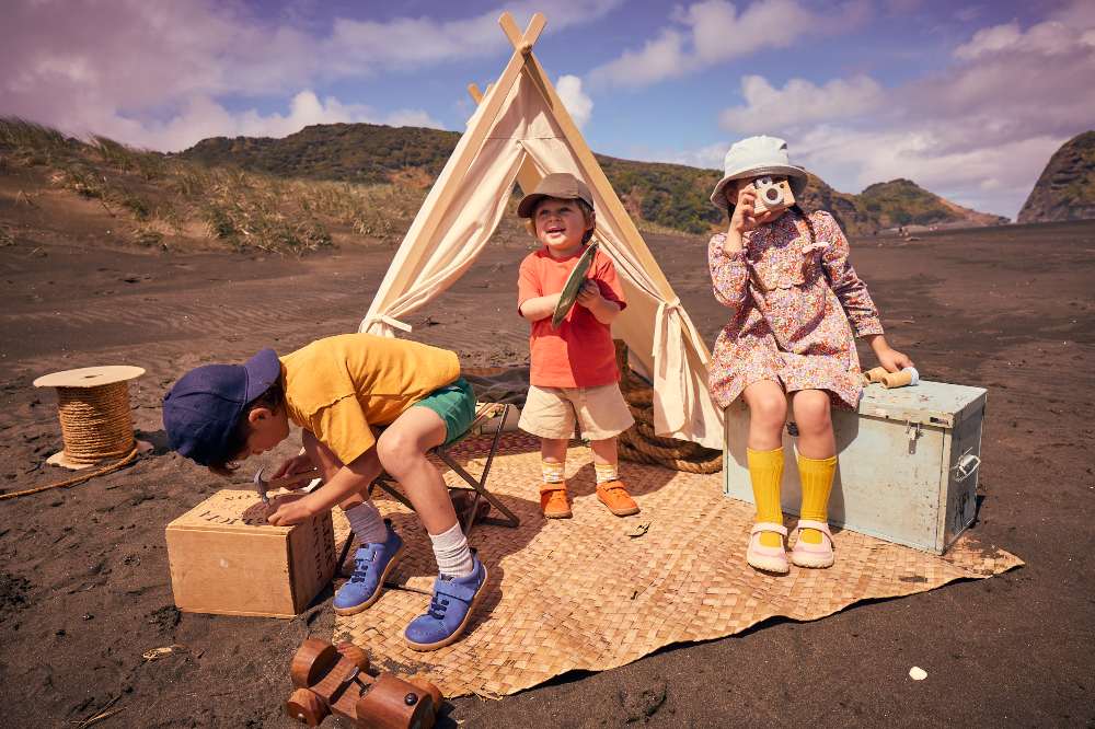 A group of children playing outside on a rug in front of a teepee