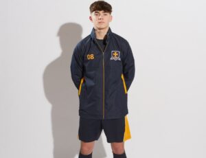 A schoolboy stood wearing a waterproof sports jacket, shorts and football socks