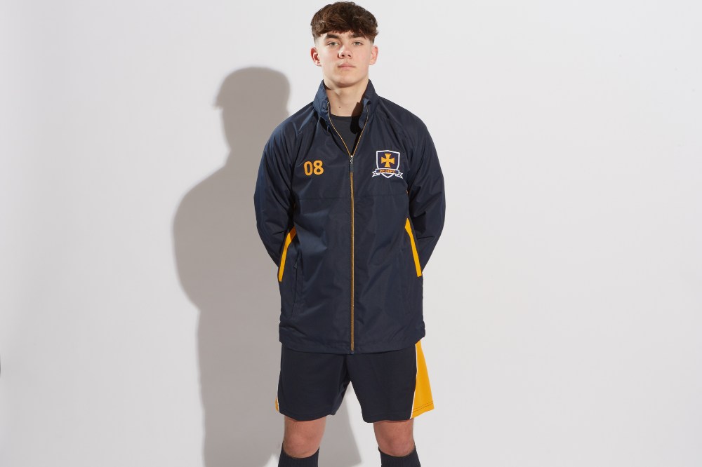 A schoolboy stood wearing a waterproof sports jacket, shorts and football socks