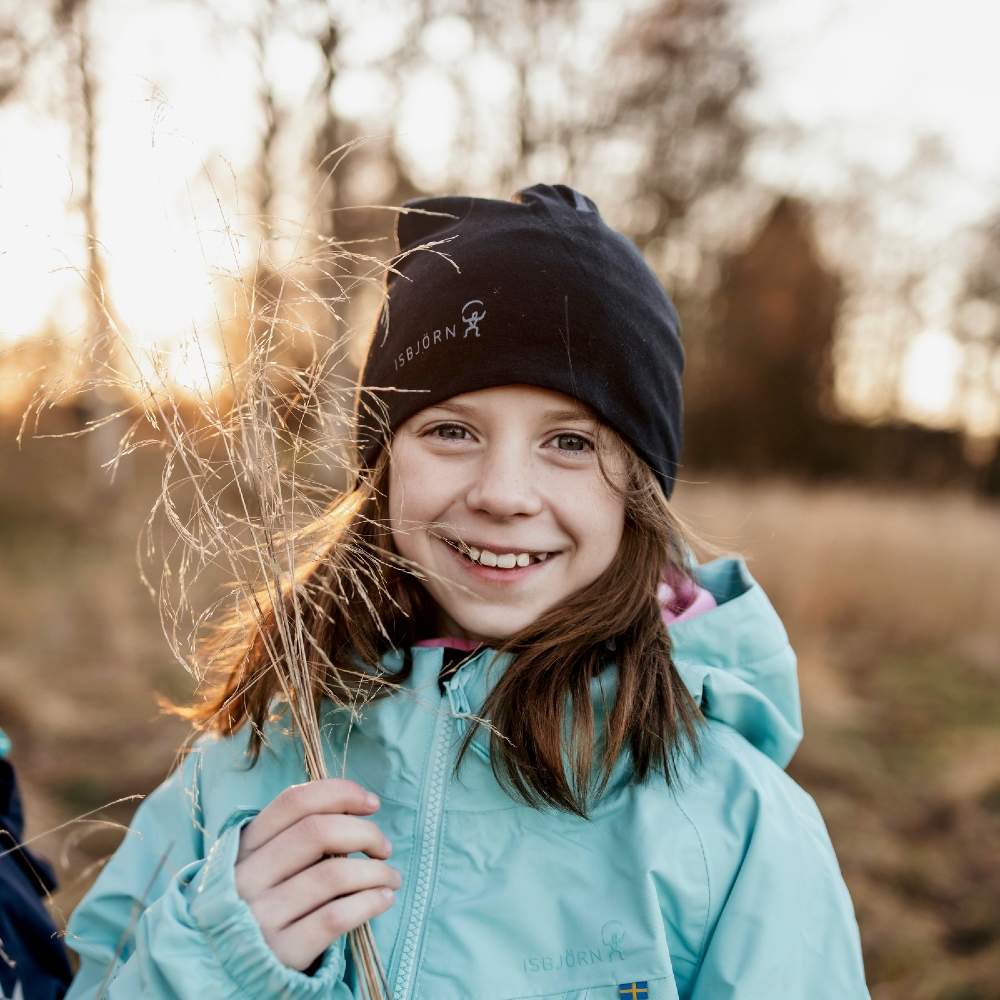 A young girl outside holding a plant wearing a black beanie hat and pale blue Monsune waterproof shell jacket by Isbjorn of Sweden