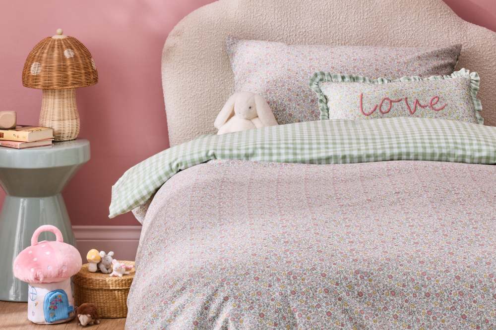 A children's bedroom with a pink floral bedding set and a side table with a mushroom light with toys on the floor