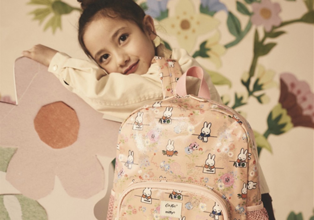 A young girl with dark hair in a bun leaning on a large pink flower cut-out with a pink rucksack on her back from the Miffy x Cath Kidston collection