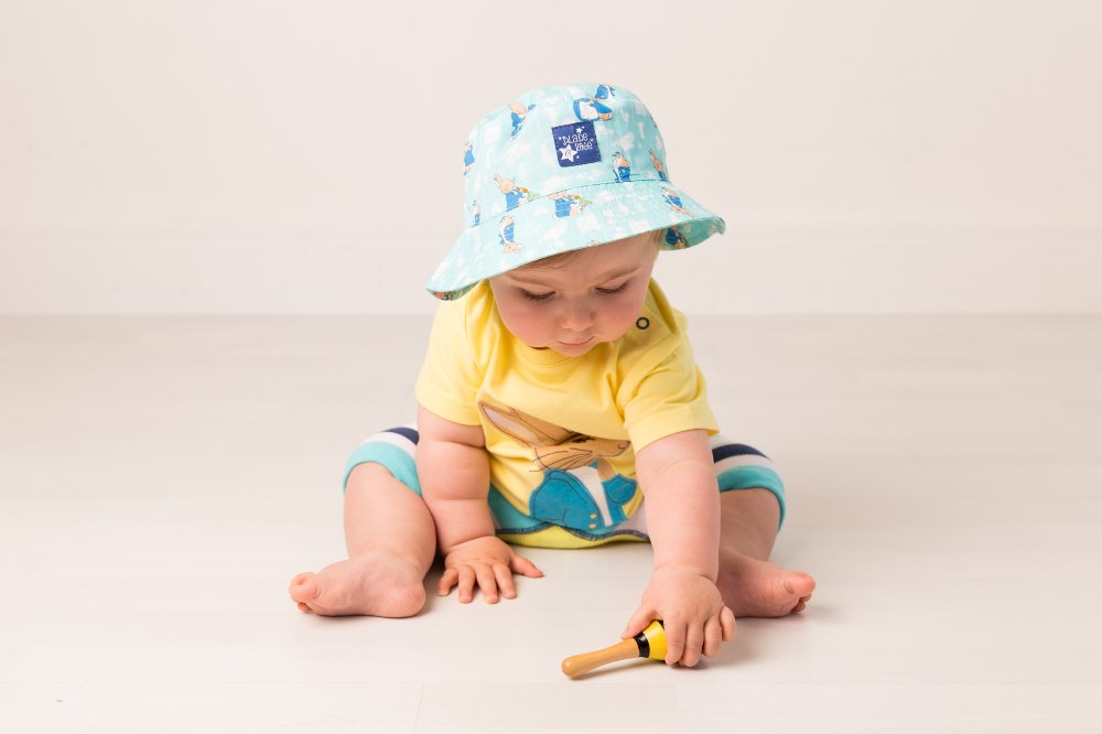 A young child in a sun hat, T-shirt and shorts by Blade & Rose playing with a toy on the floor 