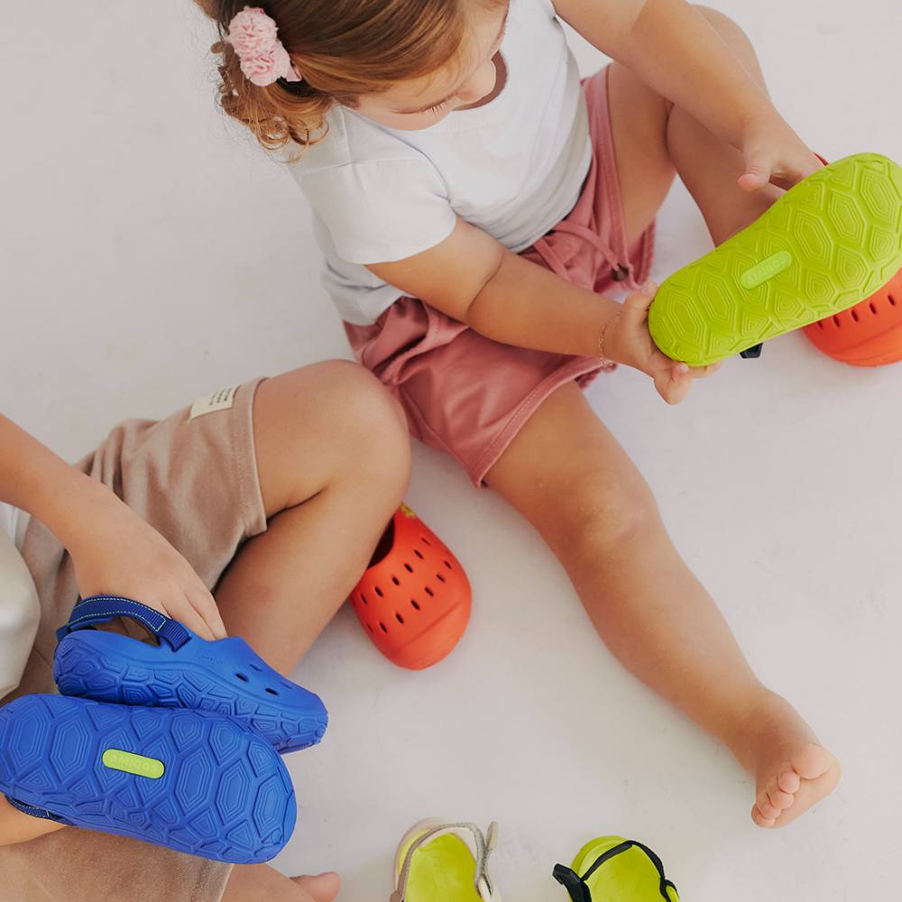 Two young children sat on the floor holding different coloured shoes 