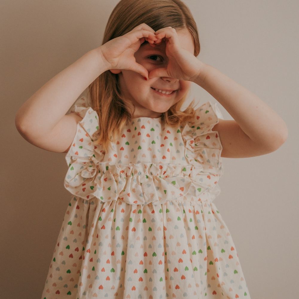 A girl in a dress holding her hands up to her face in a heart shape 