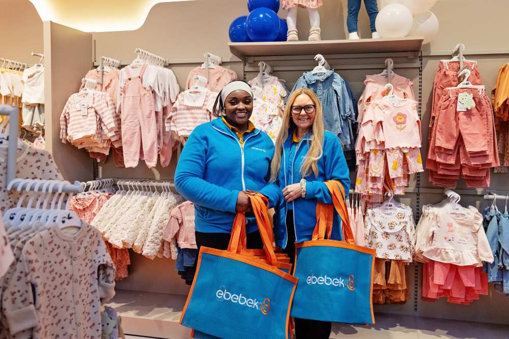 Two staff members stood in a Ebebek store in front of a display of childrenswear holding shopping bags