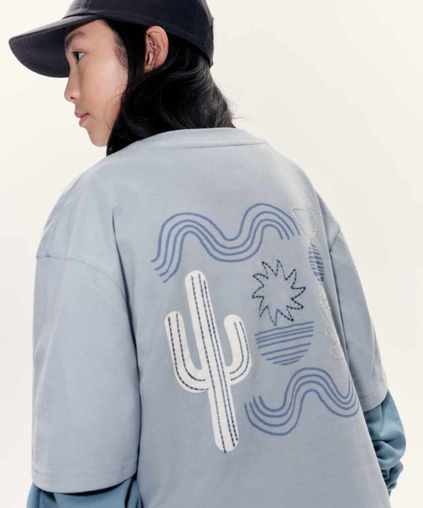 The back of a child wearing a black cap and a blue oversized jacket with embroidery on the back 