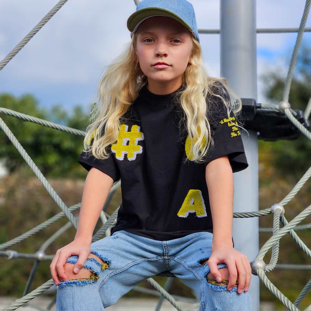 A child with long blonde hair wearing a black T-shirt and ripped jeans sat on a climbing frame 