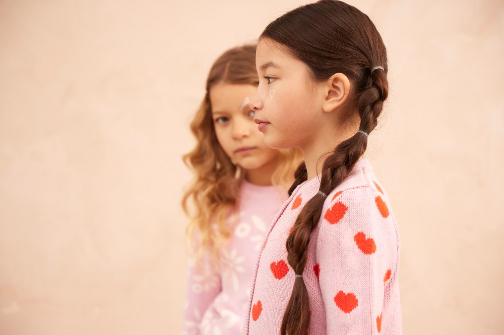 Two girls stood in a pink room wearing pink knitted jumpers 