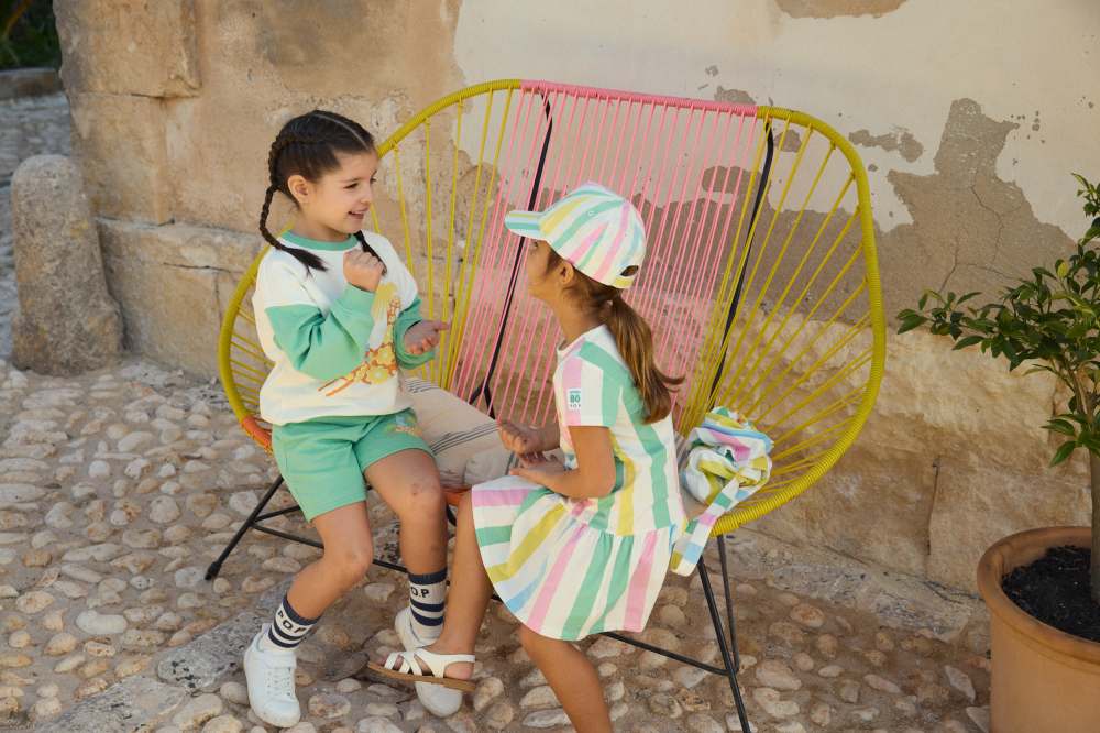 Two girls sat outside on a pink and yellow rope chair wearing outfits from PO.P's Moomins collaboration