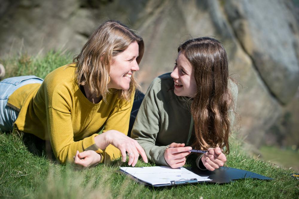 A woman and girl lying on grass on the Yorkshire moors smiling as the girl draws
