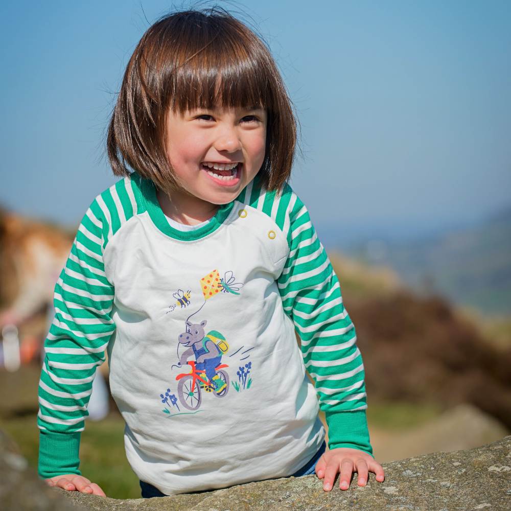 A young girl leaning on a stone wall outside wearing a top from the new More Moor collection by Ducky Zebra