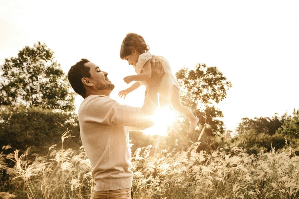 A father stood outside in a field holding a baby up