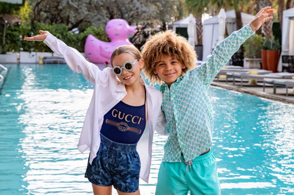 Two children stood outside in front of a pool with their arms in the air
