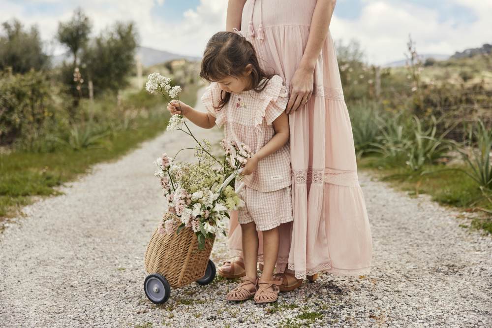 A woman outside on a path stood beside a child holding a basket trolley with flowers in it 