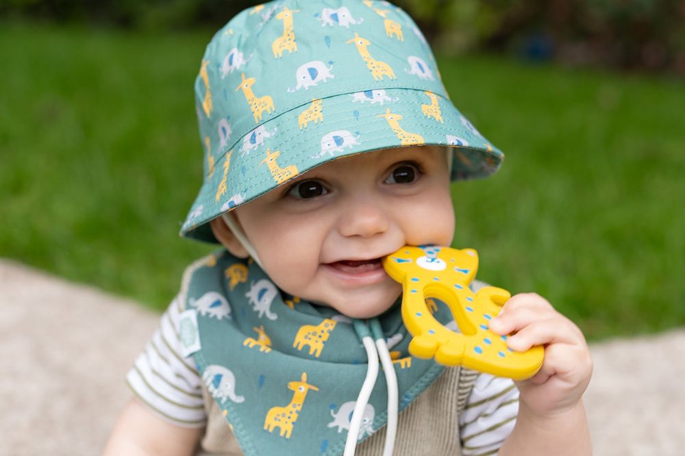 A young child sat outside in a sunhat by Ziggle and chewing a teether toy
