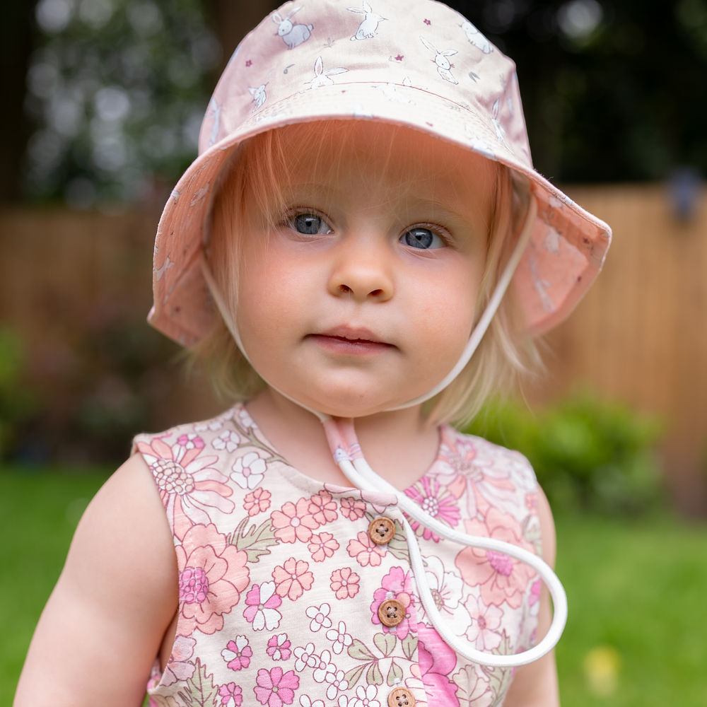 A young girl outside in a pink sunhat and dress 