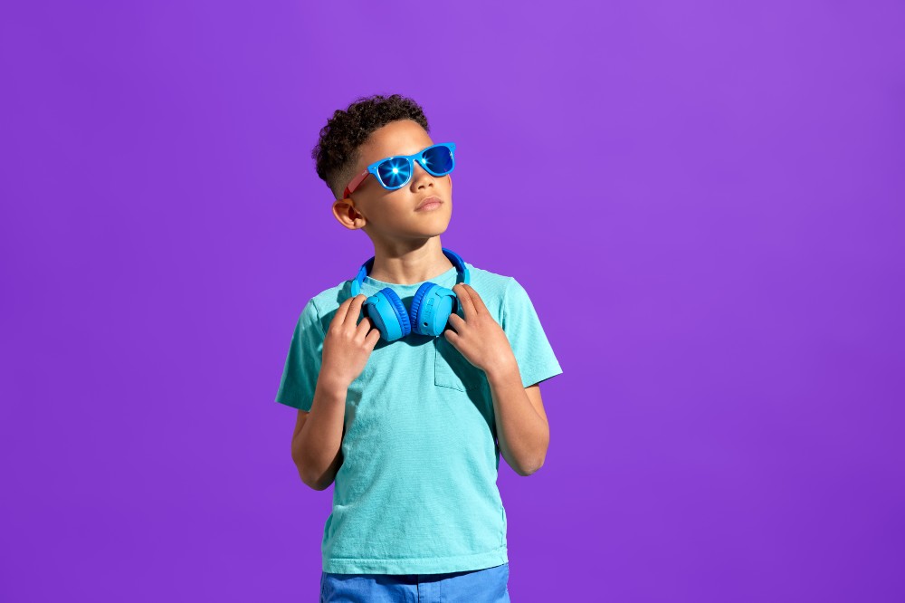 A boy stood wearing sunglasses and headphones round his neck