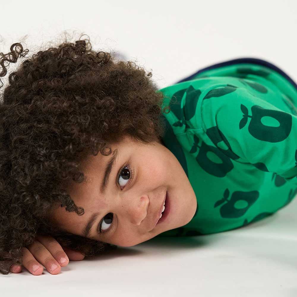 A young boy lying down wearing a green top with apple pattern